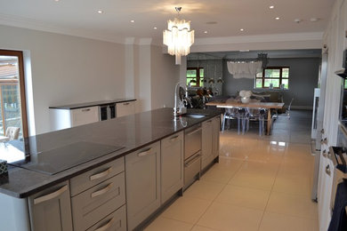 Photo of a large contemporary single-wall open plan kitchen in Cardiff with a submerged sink, flat-panel cabinets, grey cabinets, marble worktops, stainless steel appliances, ceramic flooring, an island and beige floors.