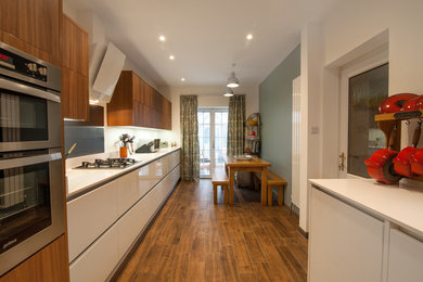 Photo of a contemporary kitchen in Dorset with flat-panel cabinets, white cabinets, integrated appliances, medium hardwood flooring, no island and brown floors.