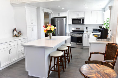 Example of a mid-sized classic u-shaped dark wood floor and wood ceiling kitchen pantry design in Los Angeles with a drop-in sink, raised-panel cabinets, white cabinets, wood countertops, white backsplash, wood backsplash, white appliances, an island and white countertops
