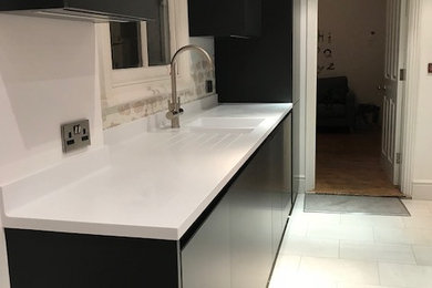 Medium sized modern galley open plan kitchen in Cambridgeshire with flat-panel cabinets, black cabinets, composite countertops, black appliances, no island and white worktops.