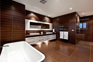 This is an example of a large modern master bathroom in Melbourne with a vessel sink, flat-panel cabinets, white cabinets, engineered quartz benchtops, a freestanding tub, an open shower, a wall-mount toilet, brown tile, porcelain tile, brown walls and porcelain floors.