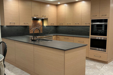 Design ideas for a large modern u-shaped eat-in kitchen in New York with an undermount sink, flat-panel cabinets, light wood cabinets, black splashback, porcelain splashback, black appliances, vinyl floors, no island and grey floor.