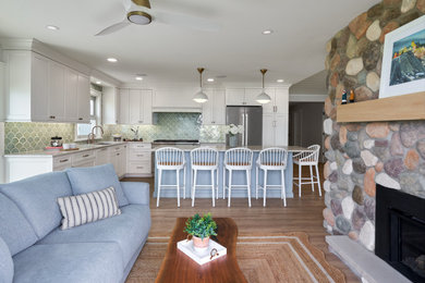 Example of a large beach style open concept medium tone wood floor, beige floor and shiplap ceiling living room design in Grand Rapids with a two-sided fireplace and a stone fireplace