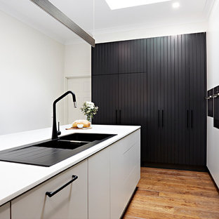 Photo of a single-wall kitchen pantry in Melbourne with a drop-in sink, beaded inset cabinets, white cabinets, marble benchtops, subway tile splashback, black appliances, plywood floors and with island.