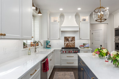 This is an example of a mid-sized transitional l-shaped eat-in kitchen in St Louis with an undermount sink, flat-panel cabinets, white cabinets, quartz benchtops, white splashback, ceramic splashback, stainless steel appliances, dark hardwood floors, with island, brown floor and white benchtop.