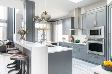 Photo of a modern l-shaped kitchen/diner in Calgary with shaker cabinets, grey cabinets, quartz worktops, white splashback, ceramic splashback, stainless steel appliances, an island and white worktops.