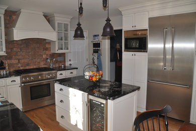 Example of a mid-sized mountain style u-shaped medium tone wood floor and brown floor eat-in kitchen design in Baltimore with a farmhouse sink, recessed-panel cabinets, white cabinets, granite countertops, red backsplash, stone tile backsplash, stainless steel appliances and an island