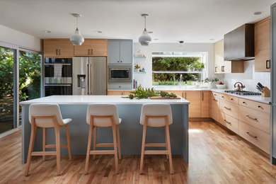 Imagen de cocina comedor actual de tamaño medio con fregadero bajoencimera, armarios con paneles lisos, puertas de armario de madera clara, encimera de cuarzo compacto, salpicadero blanco, salpicadero de azulejos de cerámica, electrodomésticos de acero inoxidable, suelo de madera en tonos medios, una isla y encimeras blancas