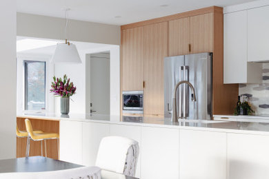 Open concept kitchen - mid-sized mid-century modern galley medium tone wood floor and brown floor open concept kitchen idea in Edmonton with a double-bowl sink, flat-panel cabinets, light wood cabinets, quartz countertops, multicolored backsplash, porcelain backsplash, stainless steel appliances, an island and white countertops