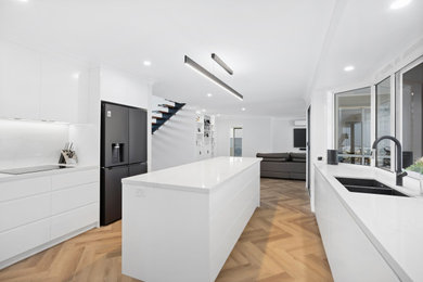 Large contemporary kitchen pantry in Gold Coast - Tweed with an undermount sink, flat-panel cabinets, white cabinets, quartz benchtops, white splashback, engineered quartz splashback, black appliances, light hardwood floors, with island, brown floor, yellow benchtop and recessed.