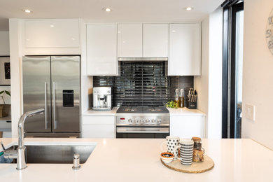 Eat-in kitchen - small contemporary galley concrete floor, gray floor and coffered ceiling eat-in kitchen idea in Vancouver with an undermount sink, flat-panel cabinets, white cabinets, solid surface countertops, black backsplash, porcelain backsplash, stainless steel appliances, an island and white countertops