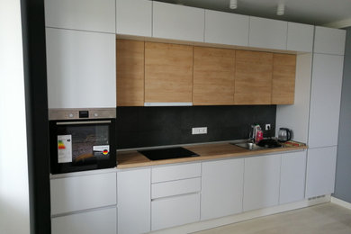 На фото: прямая кухня-гостиная среднего размера в стиле модернизм с плоскими фасадами, белыми фасадами, столешницей из ламината, черным фартуком и черной техникой с