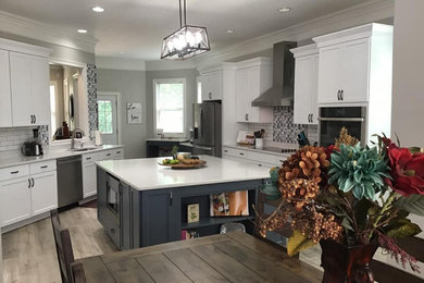 Large farmhouse galley laminate floor and gray floor eat-in kitchen photo in Nashville with an undermount sink, shaker cabinets, white cabinets, quartz countertops, white backsplash, subway tile backsplash, stainless steel appliances, an island and white countertops