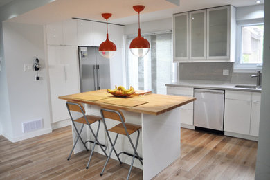 Photo of a mid-sized contemporary l-shaped kitchen in Toronto with an undermount sink, flat-panel cabinets, white cabinets, wood benchtops, grey splashback, stainless steel appliances, medium hardwood floors, with island and brown floor.