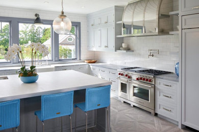 Design ideas for a large transitional l-shaped eat-in kitchen in New York with a farmhouse sink, beaded inset cabinets, grey cabinets, marble benchtops, white splashback, subway tile splashback, panelled appliances, medium hardwood floors, with island, brown floor and grey benchtop.