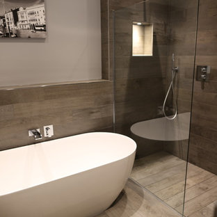 Large modern wet room in Essex with freestanding cabinets, medium wood cabinets, a freestanding bath, a wall mounted toilet, grey tiles, porcelain tiles, grey walls, porcelain flooring, a vessel sink, wooden worktops, grey floors and an open shower.