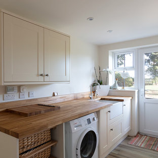 バークシャーの中サイズのトランジショナルスタイルのおしゃれな洗濯室 (エプロンフロントシンク、シェーカースタイル扉のキャビネット、ベージュのキャビネット、木材カウンター、ベージュの壁、茶色い床、茶色いキッチンカウンター) の写真
