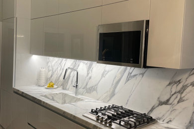 Small contemporary galley kitchen in New York with an integrated sink, flat-panel cabinets, white cabinets, marble benchtops, white splashback, marble splashback, stainless steel appliances, medium hardwood floors, no island, beige floor and white benchtop.