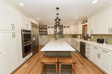 Large transitional u-shaped eat-in kitchen in Baltimore with a farmhouse sink, raised-panel cabinets, white cabinets, quartz benchtops, green splashback, glass tile splashback, stainless steel appliances, with island and white benchtop.