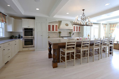 Traditional l-shaped eat-in kitchen in Cincinnati with a farmhouse sink, shaker cabinets, white cabinets, beige splashback, stainless steel appliances, light hardwood floors and with island.