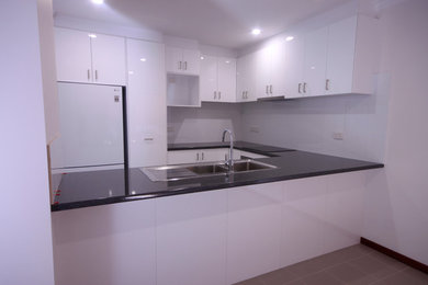 Inspiration for a mid-sized modern u-shaped eat-in kitchen in Perth with a double-bowl sink, white cabinets, laminate benchtops, white splashback, ceramic splashback, stainless steel appliances and porcelain floors.