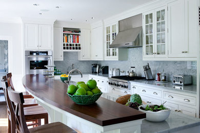 Example of a transitional l-shaped dark wood floor kitchen design in Boston with a farmhouse sink, shaker cabinets, white cabinets, marble countertops, white backsplash, stone slab backsplash, stainless steel appliances and an island