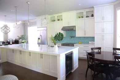 Large beach style single-wall kitchen/diner in Austin with a submerged sink, recessed-panel cabinets, white cabinets, engineered stone countertops, blue splashback, ceramic splashback, stainless steel appliances, dark hardwood flooring, an island, brown floors and white worktops.