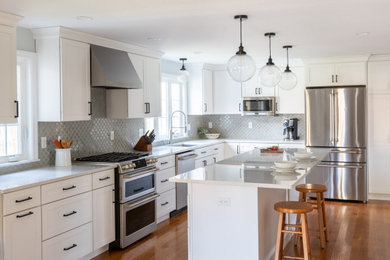 Huge transitional l-shaped medium tone wood floor and brown floor eat-in kitchen photo in Boston with an undermount sink, shaker cabinets, white cabinets, quartz countertops, gray backsplash, ceramic backsplash, stainless steel appliances, an island and white countertops