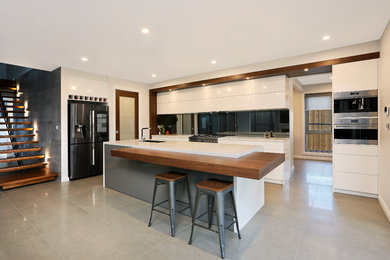 This is an example of a large contemporary galley open plan kitchen in Sydney with an undermount sink, flat-panel cabinets, white cabinets, quartz benchtops, metallic splashback, mirror splashback, stainless steel appliances, porcelain floors, with island, grey floor and white benchtop.