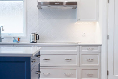Example of a large classic l-shaped medium tone wood floor open concept kitchen design in Other with an undermount sink, shaker cabinets, blue cabinets, quartz countertops, white backsplash, porcelain backsplash, stainless steel appliances, an island and white countertops