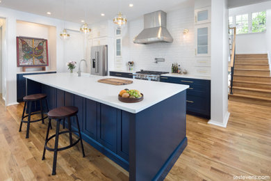 Example of a mid-sized arts and crafts l-shaped light wood floor and brown floor kitchen pantry design in Charlotte with recessed-panel cabinets, blue cabinets, white backsplash, ceramic backsplash, stainless steel appliances, an island and white countertops