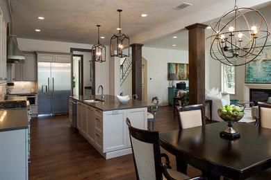 Example of a large transitional l-shaped dark wood floor eat-in kitchen design in Tampa with a double-bowl sink, recessed-panel cabinets, gray cabinets, solid surface countertops, white backsplash, stone tile backsplash, stainless steel appliances and an island