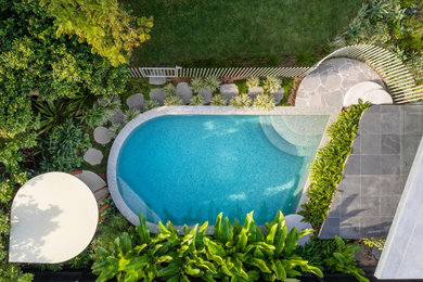 This is an example of a small tropical backyard round pool in Sydney with with a pool and natural stone pavers.