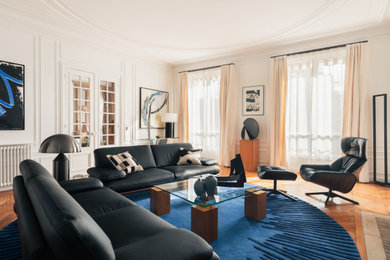 Exemple d'un salon beige et blanc tendance de taille moyenne, fermé et haussmannien avec un mur blanc, parquet clair, une cheminée standard, un manteau de cheminée en pierre, un téléviseur indépendant, un sol marron et canapé noir.