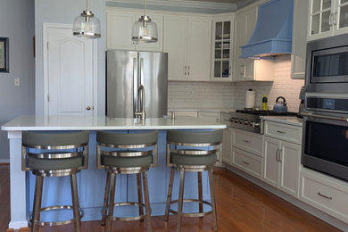 Eat-in kitchen - mid-sized transitional l-shaped medium tone wood floor and brown floor eat-in kitchen idea in Other with a farmhouse sink, shaker cabinets, white cabinets, quartzite countertops, white backsplash, subway tile backsplash, stainless steel appliances, an island and white countertops
