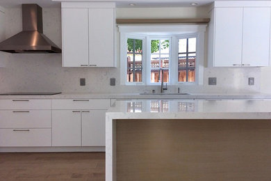 This is an example of a large modern galley eat-in kitchen in San Francisco with an undermount sink, flat-panel cabinets, white cabinets, solid surface benchtops, white splashback, stainless steel appliances, medium hardwood floors, with island and beige floor.