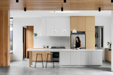 Photo of a large modern l-shaped open plan kitchen in Melbourne with a drop-in sink, flat-panel cabinets, light wood cabinets, quartz benchtops, white splashback, glass sheet splashback, stainless steel appliances, ceramic floors, with island, grey floor, white benchtop and timber.