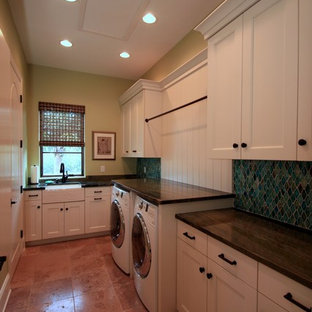 This is an example of an expansive mediterranean u-shaped separated utility room in Tampa with a belfast sink, white cabinets, granite worktops, green walls, terracotta flooring, a side by side washer and dryer, recessed-panel cabinets and brown floors.