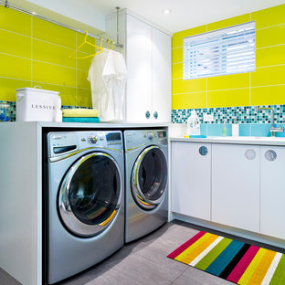 Ejemplo de cuarto de lavado actual con armarios con paneles lisos, puertas de armario blancas, paredes amarillas, lavadora y secadora juntas y suelo gris