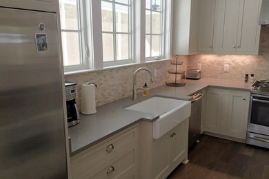Eat-in kitchen - large modern l-shaped medium tone wood floor and brown floor eat-in kitchen idea in Other with a farmhouse sink, recessed-panel cabinets, white cabinets, solid surface countertops, white backsplash, porcelain backsplash, stainless steel appliances and an island