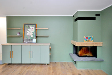 Diseño de biblioteca en casa abierta rural sin televisor con paredes verdes, suelo de madera clara, chimenea de esquina y marco de chimenea de madera