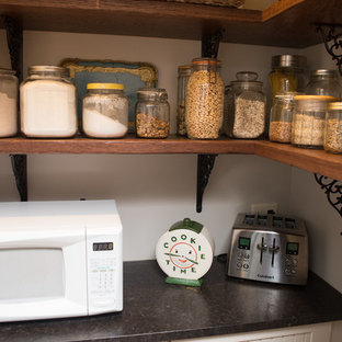 Пример оригинального дизайна: маленькая параллельная кухня в викторианском стиле с кладовкой, раковиной в стиле кантри, фасадами с утопленной филенкой, искусственно-состаренными фасадами, столешницей из гранита, бежевым фартуком, фартуком из керамической плитки, черной техникой, светлым паркетным полом, коричневым полом и черной столешницей без острова