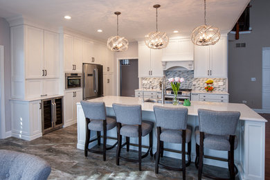 This is an example of a mid-sized transitional l-shaped open plan kitchen in Chicago with a farmhouse sink, shaker cabinets, white cabinets, quartzite benchtops, multi-coloured splashback, mosaic tile splashback, stainless steel appliances, porcelain floors, with island, brown floor and white benchtop.