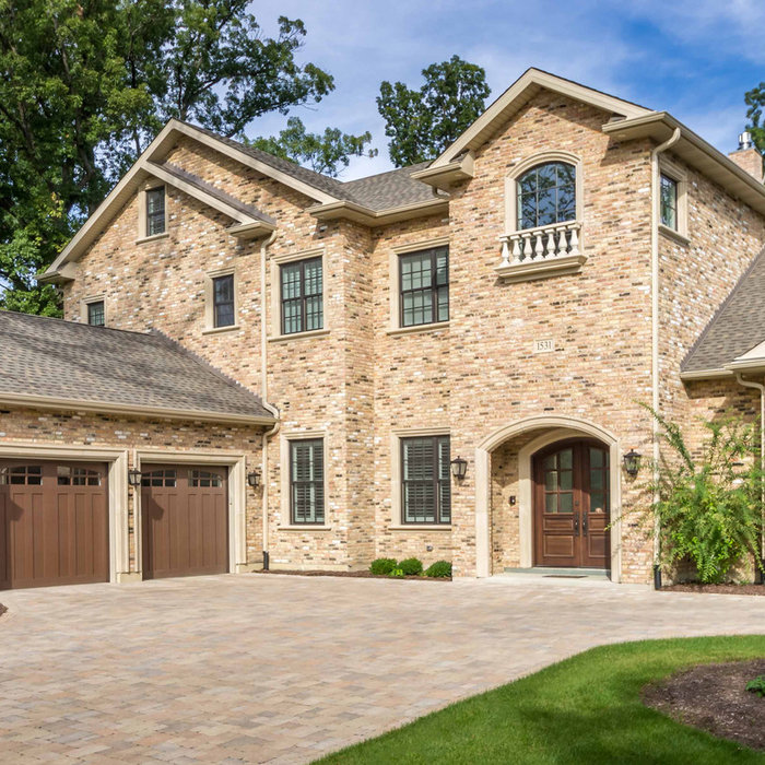 12/12-Architects-designed Elegant brick estate with arched entry, paver driveway, wood garage doors, and mature treescape.