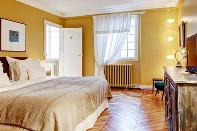 Aménagement d'une grande chambre parentale éclectique avec un mur jaune, un sol en bois brun et un sol marron.