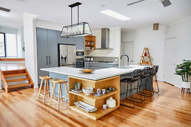 This is an example of a contemporary u-shaped open plan kitchen in Other with flat-panel cabinets, grey cabinets, grey splashback, stainless steel appliances, light hardwood floors, with island and brown floor.