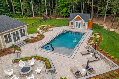 This is an example of a large modern back rectangular infinity hot tub in Bridgeport with concrete paving.