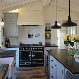 Идея дизайна: большая угловая кухня в стиле кантри с кладовкой, раковиной в стиле кантри, фасадами с утопленной филенкой, белыми фасадами, белым фартуком, фартуком из плитки кабанчик, черной техникой, темным паркетным полом, островом, столешницей из талькохлорита и коричневым полом