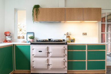 Photo of a mid-sized midcentury u-shaped eat-in kitchen in West Midlands with an integrated sink, flat-panel cabinets, green cabinets, solid surface benchtops, white splashback, glass tile splashback, coloured appliances, vinyl floors, with island, multi-coloured floor and white benchtop.