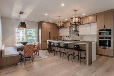 Large minimalist light wood floor and brown floor open concept kitchen photo in Cleveland with a farmhouse sink, flat-panel cabinets, light wood cabinets, quartz countertops, white backsplash, ceramic backsplash, stainless steel appliances, an island and white countertops